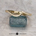 The "Calliste" band in 18K yellow gold, featuring a wavy design set with small diamonds, is displayed on a rough blue stone with the text "EARTH'S TREASURY" below.