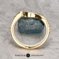 The "Calliste" band in 18K yellow gold stands upright on a gray stone atop a patterned metallic surface, with the Earth’s Treasury logo displayed below.