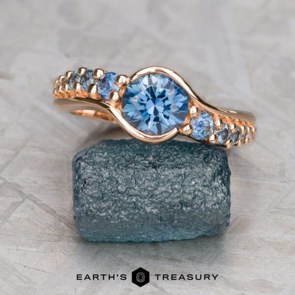The "Venus" ring in 20k pink gold with 1.06-carat Montana sapphire The "Venus" ring in 20k pink gold with a 1.06-carat Montana sapphire is displayed on a rough blue stone slab, with the Earth's Treasury logo below.