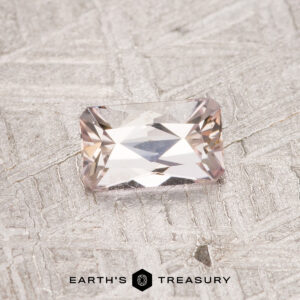 A 0.50-carat Fancy Tanzanite faceted gemstone is placed on a textured surface with the text "EARTH'S TREASURY" at the bottom.
