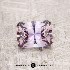 A faceted, rectangular 0.91-carat Fancy Tanzanite gemstone displayed on a textured gray surface labeled "Earth's Treasury.
