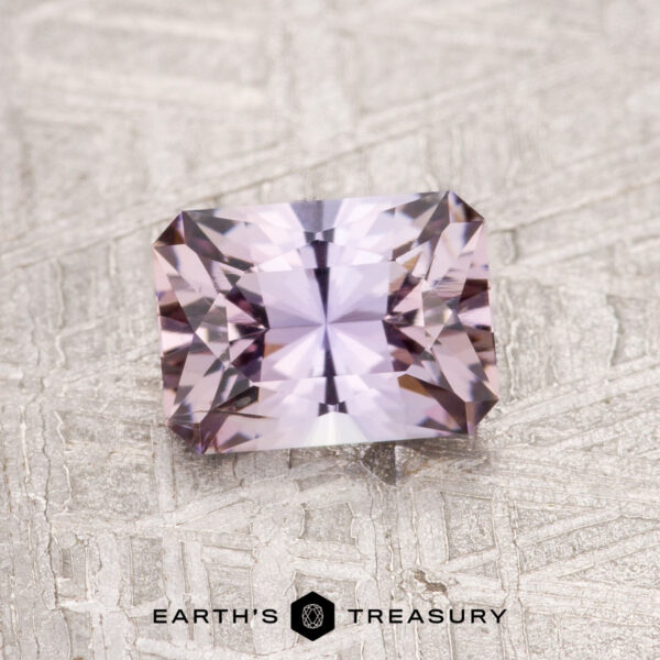 A faceted, rectangular 0.91-carat Fancy Tanzanite gemstone displayed on a textured gray surface labeled "Earth's Treasury.