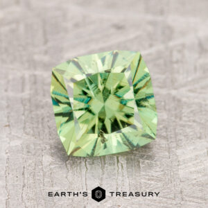 A 1.63-carat Demantoid Garnet, with square cuts and reflective facets, sits on a textured gray surface.