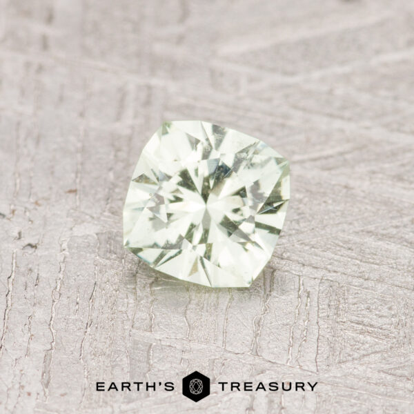 A cushion-cut pale kiwi-green gemstone, weighing 0.47 carats, resting on a textured gray surface with the "Earth's Treasury" logo at the bottom.