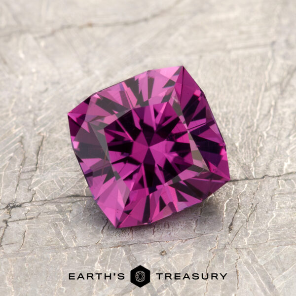1.53-Carat Magenta Purple to Intense Pink Color Change Garnet A square-cut, deep purple gemstone—ET1993—evokes the striking allure of a magenta garnet as it rests on a textured gray surface. The words "EARTH'S TREASURY" appear at the bottom of the image.