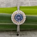 The "Victoria" Ring in 14k rose and white gold features a 1.05-carat Montana Sapphire, surrounded by a double diamond halo and diamonds on the band, displayed on a green leaf with "Earth's Treasury" at the bottom.