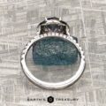 The "Victoria" Ring in 14k rose and white gold features a 1.05-carat Montana sapphire as the center stone, accented by small clear stones along the band. Displayed on a rough blue crystal with the "EARTH'S TREASURY" logo at the bottom.