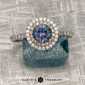 The "Victoria" Ring in 14k rose and white gold with a 1.05-carat Montana sapphire and double diamond halo sits on a rough blue stone atop a textured metallic surface. "EARTH'S TREASURY" is displayed at the bottom.