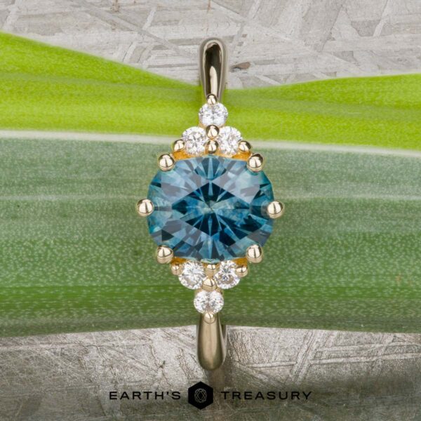 The “Mari” ring in 14k yellow gold with 1.63-Carat Montana Sapphire The “Mari” ring in 14k yellow gold features a 1.63-carat Montana Sapphire center, encircled by small diamonds and beautifully displayed on a green leaf background.