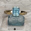 The "Freya" ring in 14k yellow gold with a 2.27-carat Montana sapphire rests on a rough blue stone atop a textured gray surface. The Earth’s Treasury logo appears at the bottom.