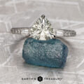 The “Adelaide” ring in 14k white gold with a 2.26-carat Montana sapphire is displayed on a blue rough stone, set against a geometric background with the "Earth's Treasury" logo below.