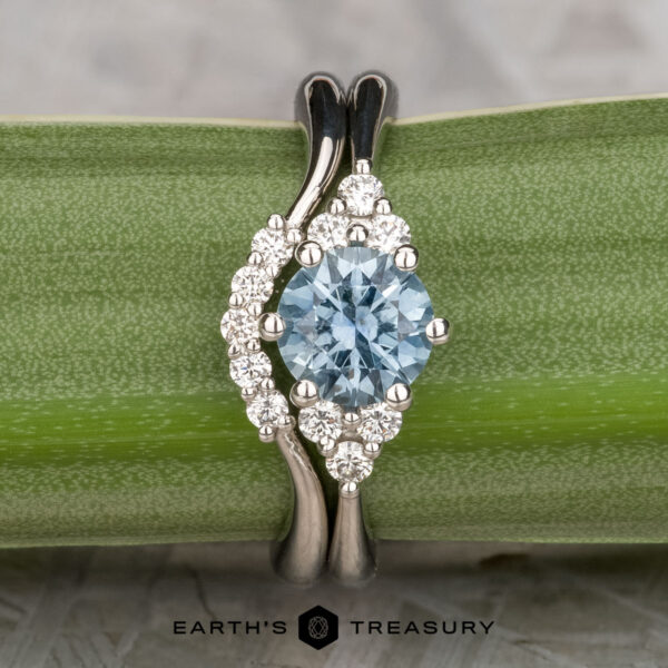 The "Mari" ring in platinum with 1.01-carat Montana sapphire, alongside th "Electra" band in platinum The "Mari" ring in platinum with a 1.01-carat Montana sapphire is shown beside the "Electra" band, both in platinum, elegantly displayed on a green plant stem.