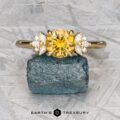 The "Surya" ring in 18k yellow gold with a 1.46-carat Montana sapphire is showcased on a rough blue stone, against a textured backdrop with "Earth's Treasury" at the bottom.