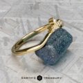 The "Surya" band in 18k yellow gold is showcased on a rough blue stone atop a textured metallic surface, with the Earth’s Treasury logo beneath.