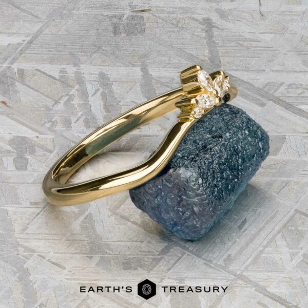 The "Surya" band in 18k yellow gold The "Surya" band in 18k yellow gold is showcased on a rough blue stone atop a textured metallic surface, with the Earth’s Treasury logo beneath.