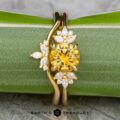 The "Surya" ring in 18k yellow gold with a 1.46-carat Montana sapphire is shown with the "Surya" band, both displayed on a green background with "Earth's Treasury" branding at the bottom.
