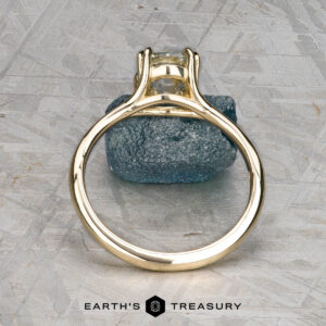 The "Daphne" ring in 14k yellow gold with a 1.71-carat Montana sapphire is shown upright on a textured blue stone, with "Earth's Treasury" branding below.