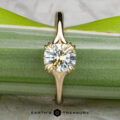 The "Daphne" ring in 14k yellow gold, set with a 1.71-carat Montana sapphire, stands upright against a green leaf background. The Earth's Treasury logo is shown below.
