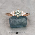 The "Mari" ring in 14k rose gold with a 0.81-carat Montana sapphire is displayed on a rough blue stone, small diamonds accenting the band, with the "Earth's Treasury" logo below.