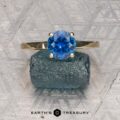 The "Freya" ring in 14k yellow gold with a 1.51-carat Montana sapphire is balanced on a rough blue crystal, set against a patterned grey background, with the Earth's Treasury logo at the bottom.
