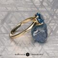 The "Freya" ring in 14k yellow gold, featuring a 1.51-carat Montana sapphire, is showcased beside a raw blue mineral on a gray patterned surface. The text "EARTH'S TREASURY" appears at the bottom.