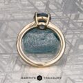 The "Freya" ring in 14k yellow gold with a 1.51-carat Montana sapphire is shown upright on rough blue mineral, with a patterned metallic background and the "Earth's Treasury" logo at the bottom.