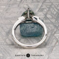A Roe, Ana Ring featuring a silver band with a green gemstone stands upright on a textured metallic surface, with "EARTH'S TREASURY" displayed below.