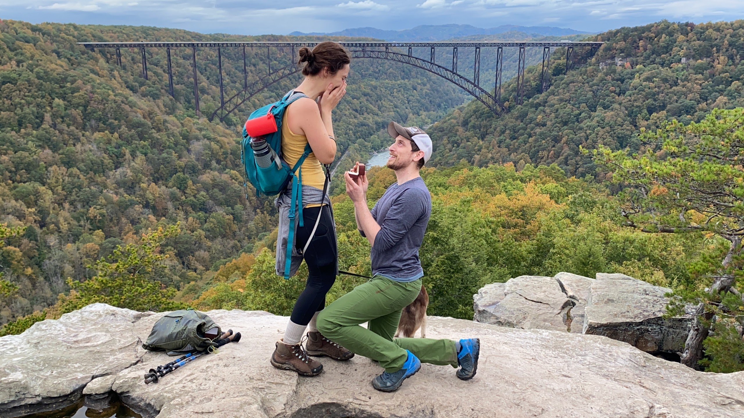 A photo from a customer review of a couple in hiking gear on a cliff overlooking scenic forest and river