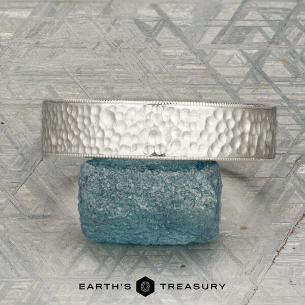The "Rainier" ring in platinum The "Rainier" ring in platinum is displayed upright on a rough blue stone, with a geometric patterned background and the "Earth's Treasury" logo below.
