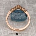 The "Melilai" band in 20k pink gold, featuring a crown-like design, stands upright against a rough blue gemstone with the Earth's Treasury logo below.