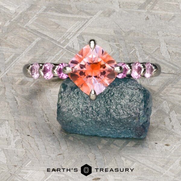 The "Dahlia" ring in platinum with 2.14-Carat Montana Sapphire The "Dahlia" ring in platinum features a 2.14-carat Montana sapphire, accented by smaller stones and displayed on a rough blue-green mineral atop a textured gray surface. Logo reads "Earth's Treasury.