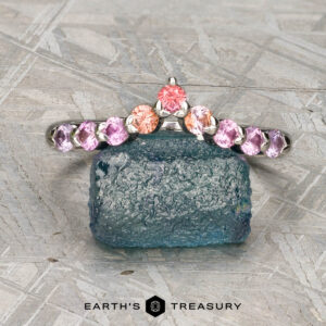 The "Dahlia" band in platinum, set with pink and orange gemstones, is shown on a rough blue stone. The text "Earth's Treasury" appears at the bottom.