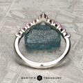 The "Dahlia" band in platinum, adorned with pink gemstones, stands upright before a rough blue crystal on a textured gray surface. "EARTH'S TREASURY" appears at the bottom.
