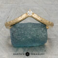 The "Passiflora" band in 18K yellow gold features engraved leaf patterns and a small central diamond, displayed upright on rough blue stone. Inspired by Earth's Treasury Passiflora Band; logo shown at the bottom.
