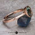 The “Luella” ring in 14k rose gold with a 2.30-carat Montana Sapphire is displayed on a rough blue stone against a textured background, with the "Earth's Treasury" logo at the bottom.