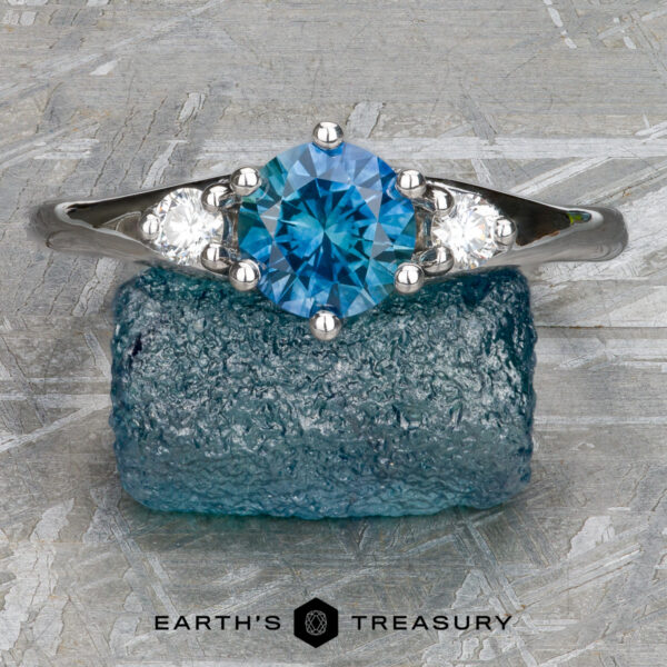 Stacked from 52 images. Method=B (R=1,S=4) A "Stacked from 52 images. Method=B (R=1,S=4)" silver Halley Ring with a blue gemstone center and two clear side stones is shown on rough blue crystal, with "Earth's Treasury" text at the bottom.
