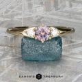 Stacked from 49 images. Method=B (R=8,S=4)" ring, showcasing a round pink center stone and two clear side stones, rests on rough blue crystal above the "Earth's Treasury" logo—a modern twist on the classic three-stone style.