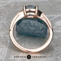 A "Niamh" ring in 14k rose gold with a 0.95-carat Montana sapphire is displayed upright on a rough blue mineral specimen, with the "Earth's Treasury" logo and text below.