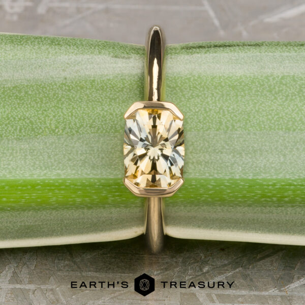 The “Larisa” ring in 18k yellow gold with 1.35-Carat Montana sapphire The “Larisa” ring in 18k yellow gold with a 1.35-carat Montana sapphire is displayed upright against a green textured background with the "Earth's Treasury" logo at the bottom, highlighting its elegance.