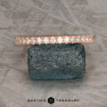 The petite pave diamond band in 14k rose gold, hammered and brushed, rests on a rough dark stone with a textured gray background. "Earth's Treasury" logo appears below.