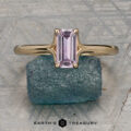 The "Phoebe" ring in 14K yellow gold, featuring a 0.73-carat Montana sapphire, is displayed on a rough blue stone atop a textured gray surface with the text "Earth's Treasury" below.