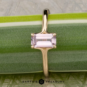 The "Phoebe" ring in 14K yellow gold, featuring a 0.73-carat Montana sapphire, rests on a green surface with the text "EARTH'S TREASURY" at the bottom.