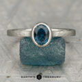 The "Luella" ring in platinum with a 1.15-carat Montana sapphire is displayed upright on a rough blue stone, with the "Earth's Treasury" logo and text below.