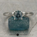 The "Phoebe" ring in platinum, featuring a 1.12-carat Songea sapphire, sits atop a rough blue crystal on a textured surface. "Earth's Treasury" is written below.