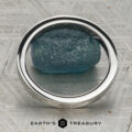The Classic Channel-Set Band in platinum, featuring a row of round diamonds, stands upright on a rough blue gemstone against a geometric background with the Earth’s Treasury logo below.