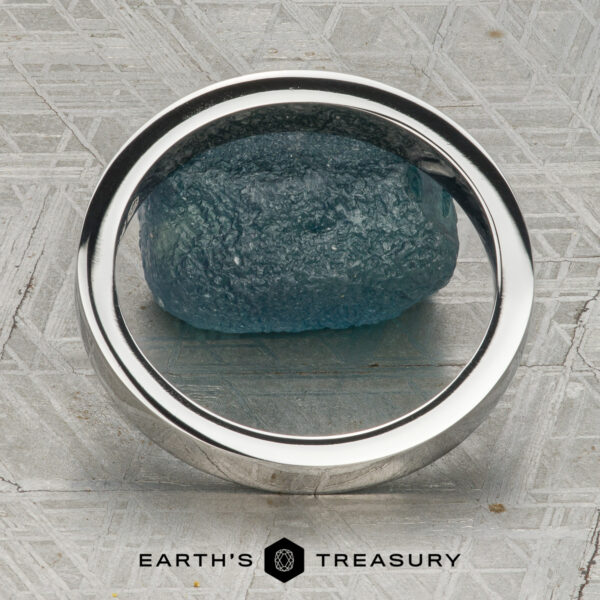 The Classic Channel-Set Band in platinum The Classic Channel-Set Band in platinum, featuring a row of round diamonds, stands upright on a rough blue gemstone against a geometric background with the Earth’s Treasury logo below.