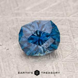 A 1.50-carat Rich Blue Montana Sapphire (Heated) rests elegantly on a white surface, its deep blue hue captivating the eye.