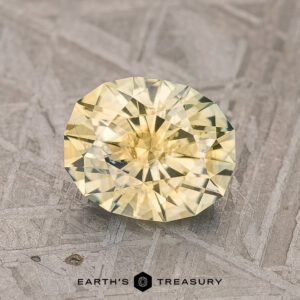 A 1.90-carat Dusky Yellow Montana Sapphire (Heated), cut in an oval facet, is elegantly displayed on a textured gray surface.