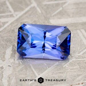 A 2.08-carat medium blue tanzanite with intricate facets, set against a textured gray background. The text "Earth's Treasury" appears at the bottom.