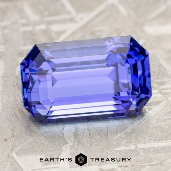 4.85-Carat Violet Blue Tanzanite (Heated) A 4.85-carat Violet Blue Tanzanite (Heated) gemstone, rectangular and faceted, rests on a textured surface with the text “EARTH'S TREASURY” beneath it.